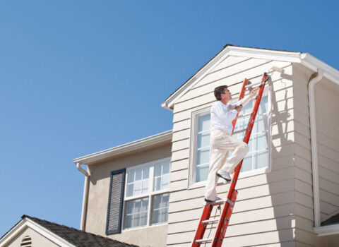 painting contractor on red ladder painting home ivory Advanced Exteriors Denver